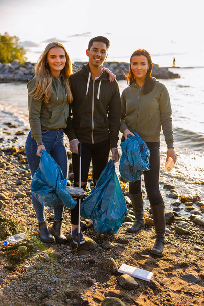 Sorrindo voluntários amigos segurando saco de lixo na praia - Foto, Imagem