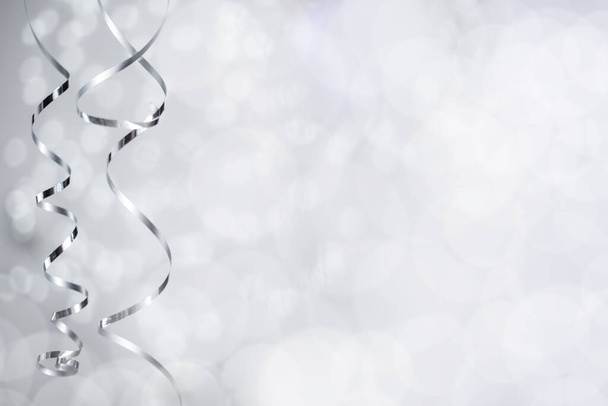 Zilveren kerst nieuwjaar krullende streamer lint over glinsterende bokeh lichten achtergrond met kopieerruimte voor tekst - Foto, afbeelding