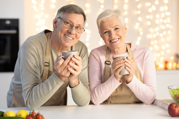 Счастливая старшая пара, пьющая кофе, празднуя Рождество, сидя на кухне - Фото, изображение
