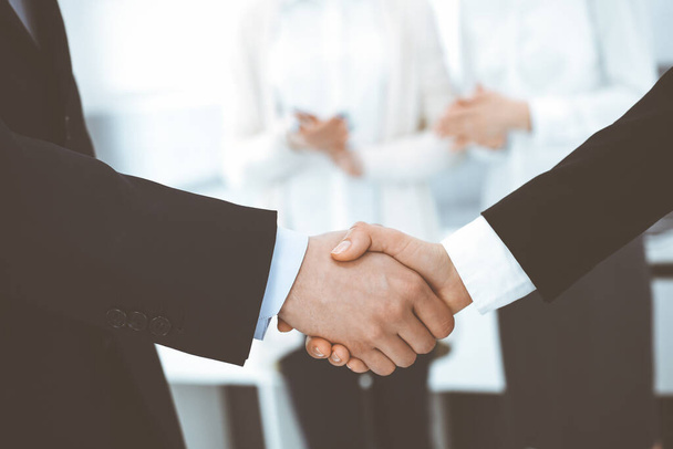 Businessman and woman shaking hands with colleagues at the background. Handshake at meeting in office. Concept of success in business - Foto, Bild
