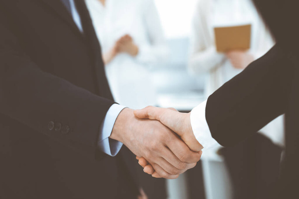 Businessman and woman shaking hands with colleagues at the background. Handshake at meeting in office. Concept of success in business - Фото, зображення
