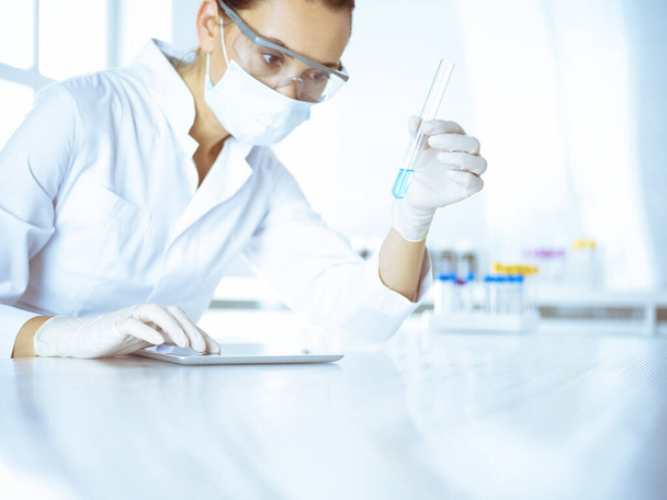 Female laboratory assistant analyzing test tube with blue liquid. Medicine, health care and researching concept - Foto, imagen