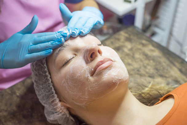Esteticista com luvas lava o rosto de uma jovem mulher. Remoção de cosméticos. Procedimentos cosméticos no salão de beleza. - Foto, Imagem