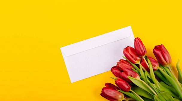 Sobre de certificado de regalo blanco sobre fondo amarillo con un ramo de tulipanes rojos y un lugar libre para el texto. Muestra de tarjeta de visita o invitación. Feliz día de San Valentín 14 de febrero. Día de la Mujer 8 de marzo. - Foto, imagen