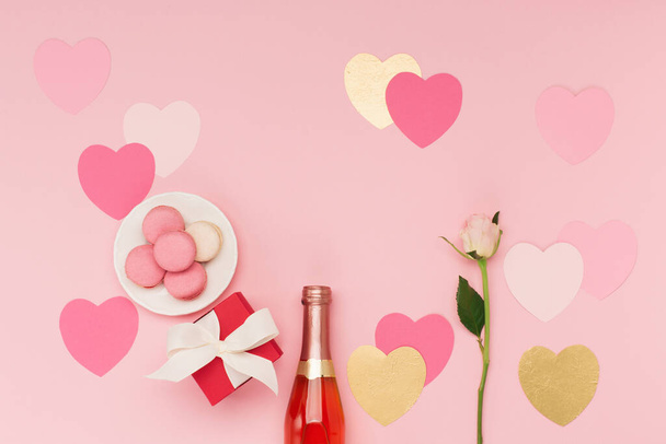 Feestelijke kerstkaart voor Valentijnsdag, Verjaardag, Vrouw of Moederdag. Roze hartjes, fles wijn, snoep en cadeau op roze achtergrond. Valentijnsdag concept. Vlakke lay, bovenaanzicht, kopieerruimte. - Foto, afbeelding