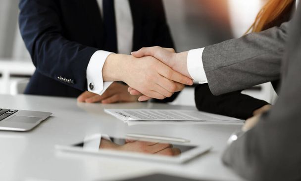 Hombre de negocios desconocido estrechando la mano con su colega o compañero por encima del escritorio en la oficina soleada, primer plano - Foto, imagen