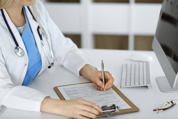 Unknown woman-doctor at work filling up medication history record form in clinic, close-up of clipboard - Photo, Image