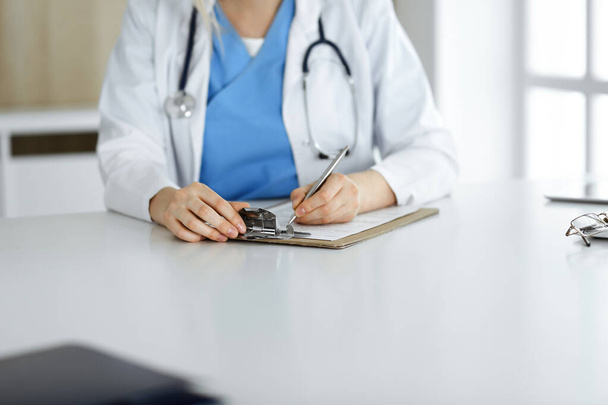 Unknown woman-doctor at work filling up medication history record form in clinic, close-up of clipboard - Foto, imagen