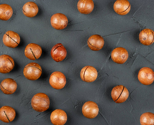 Noix de macadamia éparpillées dans leur coquille sur un fond de béton foncé, vue de dessus - Photo, image