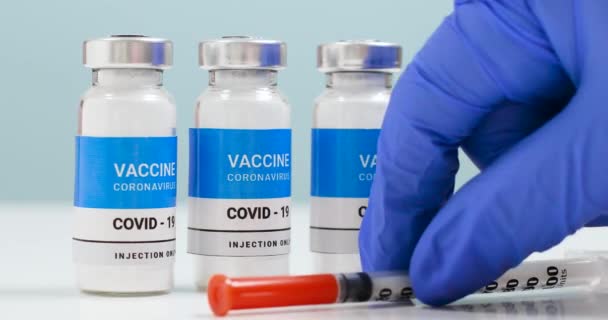 Női orvos kezek kék orvosi kesztyű átlátszó folyékony koronavírus vakcina palack és fecskendő injekció a laboratóriumban. - Felvétel, videó