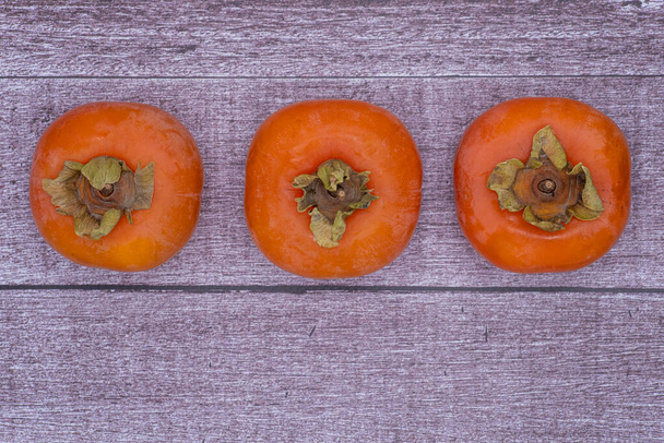 Ripe persimmons fruit on the wooden background, top view - Foto, imagen