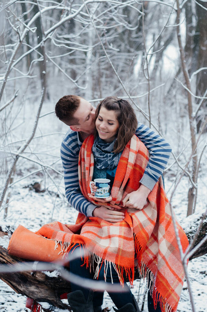 Ο άντρας φιλάει μια όμορφη γυναίκα στο χειμερινό δάσος. Μεσήλικας άντρας και γυναίκες τυλιγμένοι σε καρό. Ιστορία αγάπης - Φωτογραφία, εικόνα
