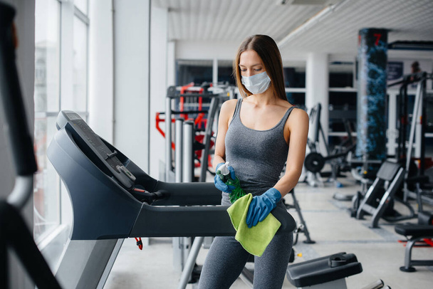The girl in the mask disinfecting the gym equipment during a pandemic. - Фото, зображення