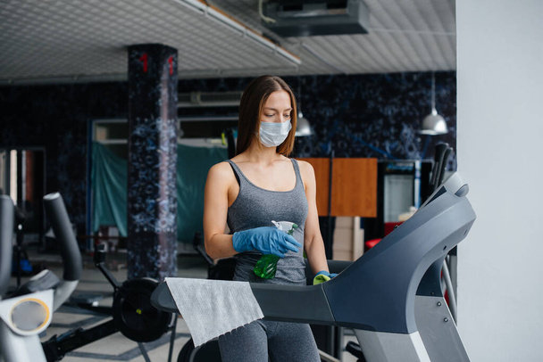 The girl in the mask disinfecting the gym equipment during a pandemic. - Foto, Imagen