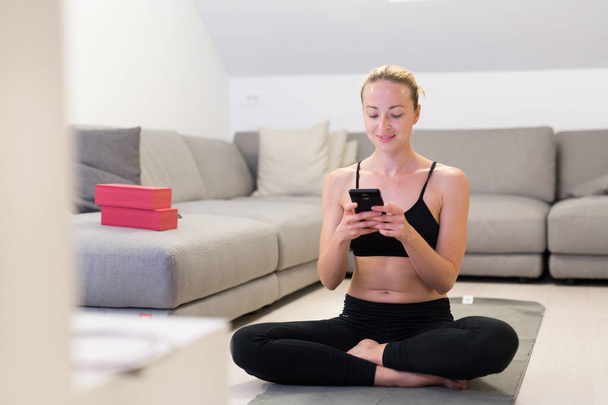 Beautiful blonde woman doing home workout indoors. Woman practice yoga at home. Fit girl using workout tutorials for healthy active lifestyle. Woman using quarantine for home workouts. - Foto, afbeelding