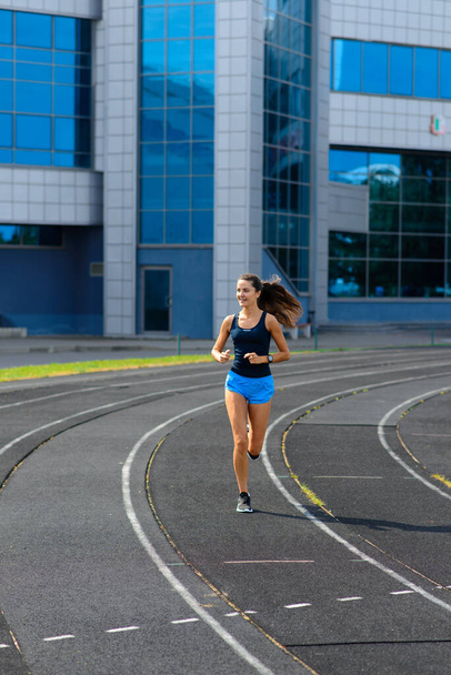 Athlete runner running on athletic track training her cardio. Woman jogging for competition race at summer outdoor stadium. - Photo, Image