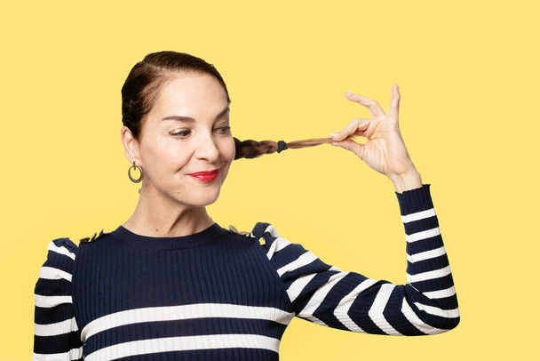 Slim woman with funny face pulling her hair over yellow background - Foto, Bild