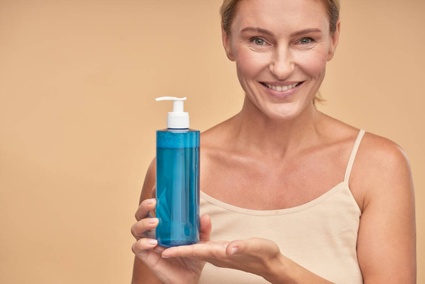 Señora sonriente sosteniendo agua micelar en botella en el estudio - Foto, imagen