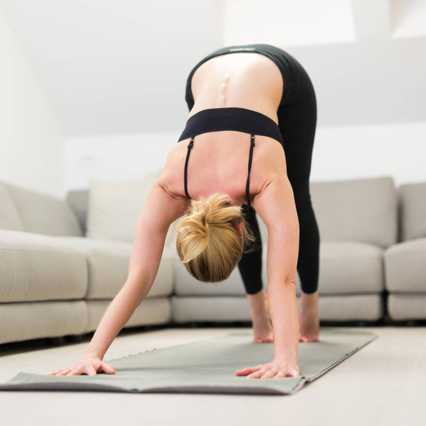 Beautiful blonde woman doing home workout indoors. Woman practice yoga at home. Fit girl using workout tutorials for healthy active lifestyle. Woman using quarantine for home workouts. - Photo, Image