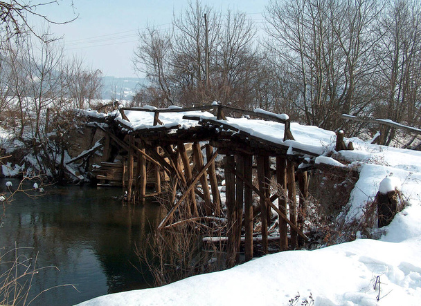 Χειμώνας. Απομεινάρια μιας παλιάς ξύλινης γέφυρας κάτω από το χιόνι. Ποταμός Mlava στην ανατολική Σερβία κοντά στην Πέτροβατς. - Φωτογραφία, εικόνα