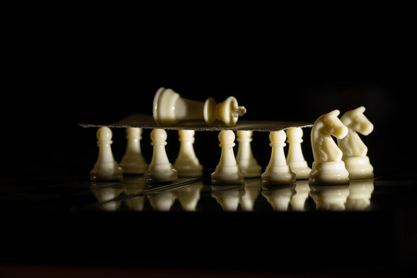 fehér sakkfigurák egy táblán fekete alapon, sakkozás - Fotó, kép