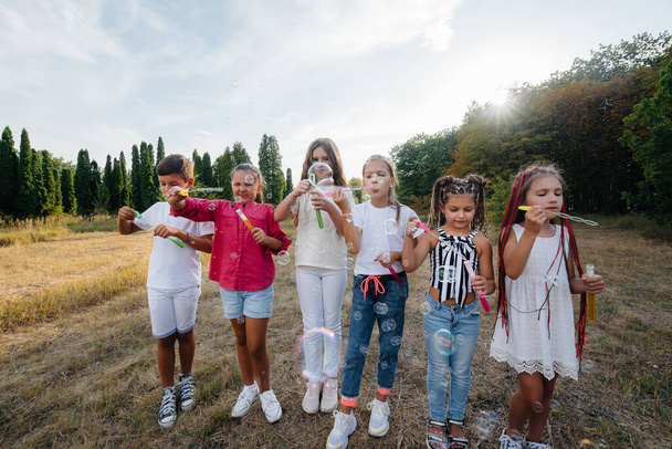 A large group of cheerful children play in the Park and inflate soap bubbles. Games in a children's camp - 写真・画像