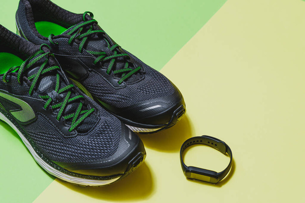 горизонтальное изображение пары черно-зеленой спортивной обуви и смарт-браслет с зеленым и желтым фоном с копировальным пространством в правом верхнем углу - Фото, изображение