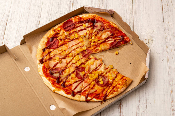Pizza in a cardboard box on a white wooden background. - Фото, зображення