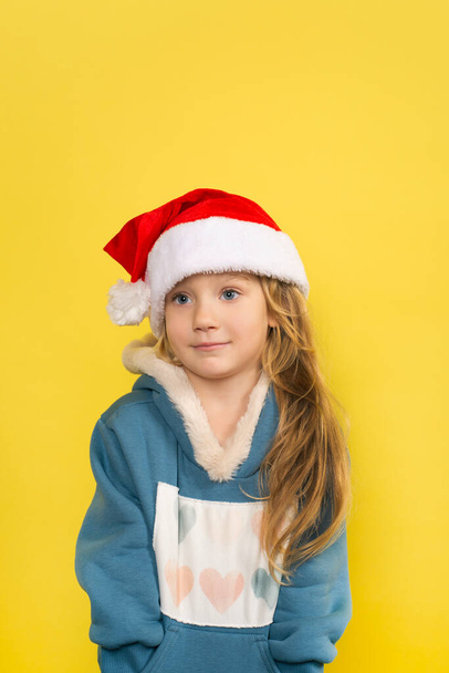 Little beautiful girl in santa hat smiling isolated on yellow background. Close up portrait. New year concept - Foto, Imagen