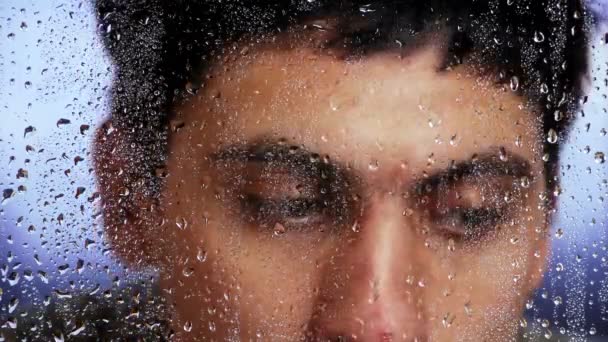 Der Typ mit dem kaukasischen Aussehen blickt nach einem Regen durch ein nasses Fenster. Nahaufnahme. - Filmmaterial, Video