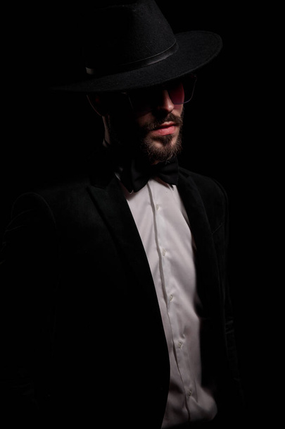 jeune homme d'affaires de mode posant sur fond noir et regardant de côté en studio - Photo, image