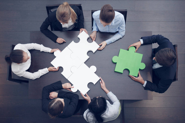 Groep van zakenmensen monteren puzzel op kantoor tafel, top view, team ondersteuning en hulp concept, groene en witte stukken - Foto, afbeelding
