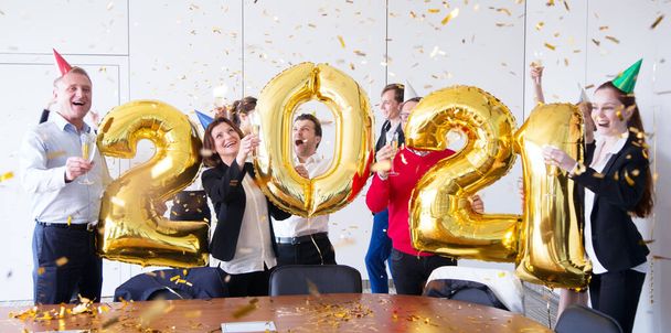 Business people are celebrating holiday in modern office drinking champagne and having fun in coworking. Merry Christmas and Happy New Year 2021. Balloon numbers - Foto, imagen