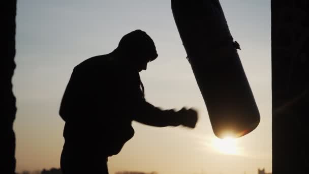 Silhouette d'un boxeur sur fond de coucher de soleil. Battre sac de poinçonnage à l'échec. Fatigue après l'entraînement - Séquence, vidéo