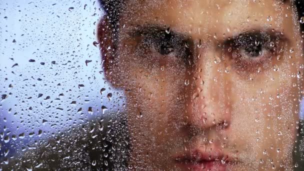 Facet o wyglądzie kaukaskim spogląda przez mokre okno po deszczu. Zbliżenie. - Materiał filmowy, wideo