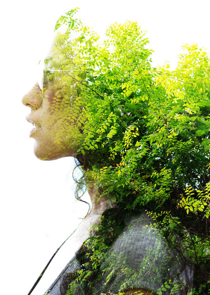 A double exposure portrait of a young woman profile with sun glasses against white background with a green tree - 写真・画像