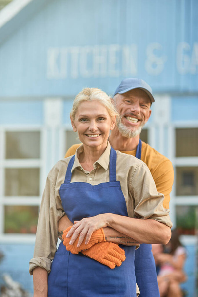 Középkorú fehér férfi ölelés boldog nő kötényben - Fotó, kép