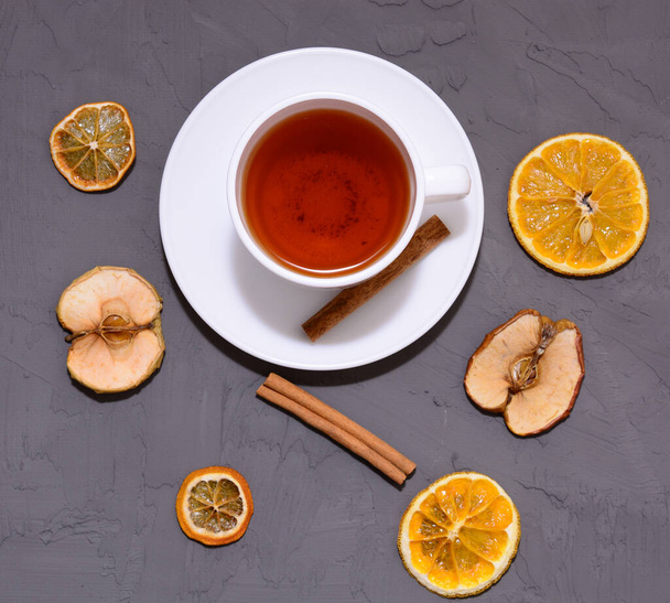 top view of Cup of tea, dried slices of orange and cinnamon with Christmas decorations on a gray wooden background. copy space. - Foto, imagen