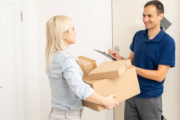 woman receiving boxes from postman at the door in home delivery concept. Woman received the parcel from the postman at home. Postman giving cardboard box to young woman. - Фото, изображение