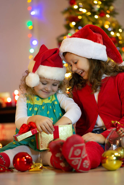 Two little girls in Santa Claus Hat with presents on Christmas party - Fotó, kép