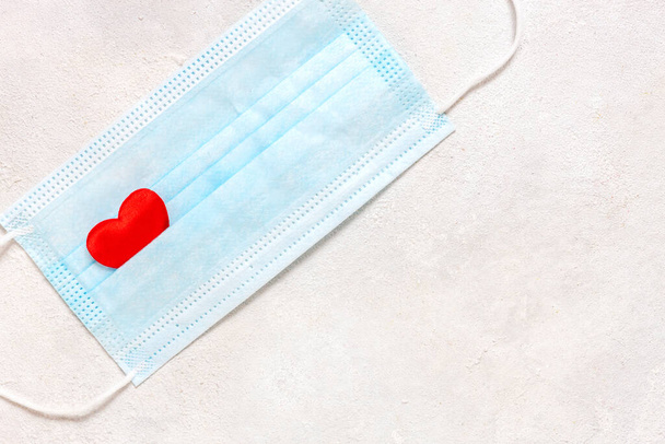Disposable protective covid face mask with red heart on a white  background. Safe Valentine`s day concept during coronavirus pandemic and social distancing  . Top view, copy space - Fotó, kép