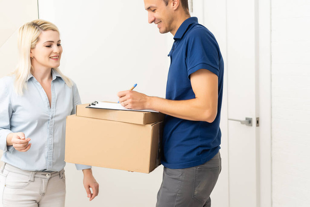 woman receiving boxes from postman at the door in home delivery concept. Woman received the parcel from the postman at home. Postman giving cardboard box to young woman. - Photo, Image