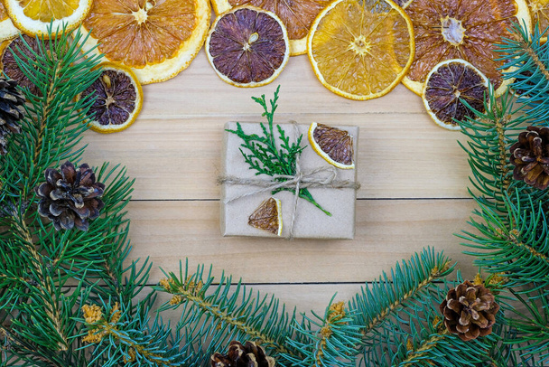 A small box on the background of Christmas tree branches and dried oranges. New Year theme. Gifts for the New Year. Christmas tree branches with cones and mugs of dried citrus fruits. - Φωτογραφία, εικόνα