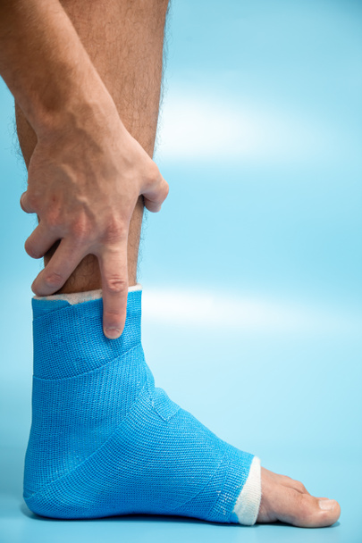 Blauer Schienenknöchel. Bandagiertes Bein auf männlichem Patienten auf hellblauem, verschwommenem Hintergrund. Sportverletzungskonzept. - Foto, Bild