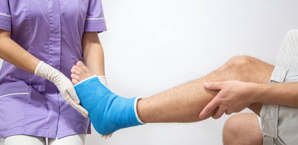 Acercamiento de la pierna de un hombre en un yeso y una férula azul después de vendar en un hospital. - Foto, Imagen