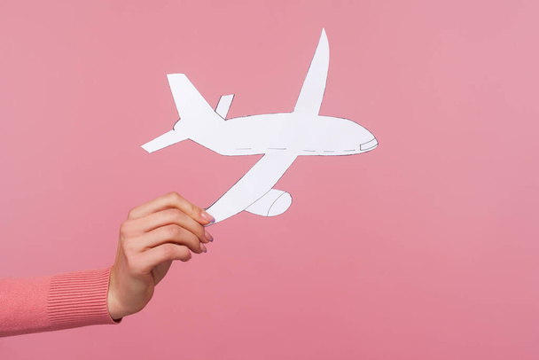 Closeup female hand holding paper plane, plane arrival and departure, travelling abroad, airline service. Indoor studio shot isolated on pink background - Фото, изображение