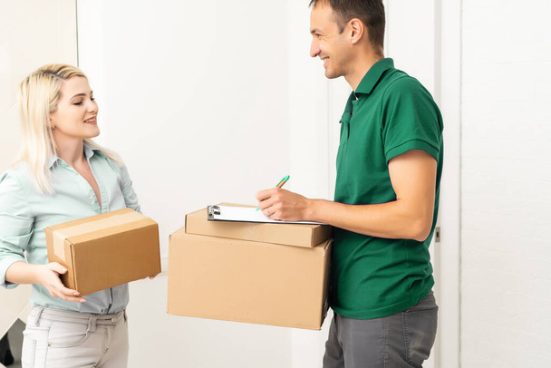 woman receiving boxes from postman at the door in home delivery concept. Woman received the parcel from the postman at home. Postman giving cardboard box to young woman. - Photo, Image