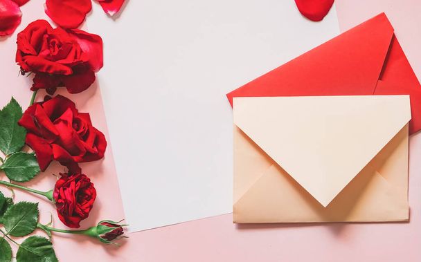 Çiçekler posta zarfındaki kırmızı güller ve pembe kağıtta yazılı yazı için boş sayfaları olan boş kağıtlar. Üst manzara, düz uzanma - Fotoğraf, Görsel