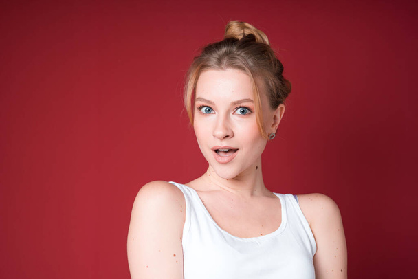 A portrait of young blond woman with a bun amazed in white tank top on cherry background. - Фото, зображення