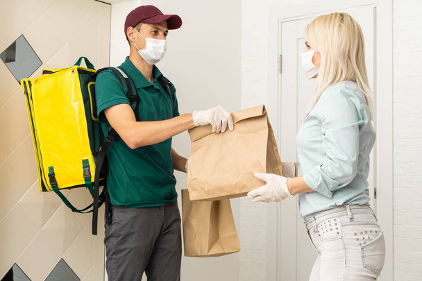 Zusteller von Waren und Paketen an Kunden, indem er sie mit medizinischen Masken und Handschuhen schützt. Online-Bestellung unter Quarantäne Coronavirus covid-19 - Foto, Bild